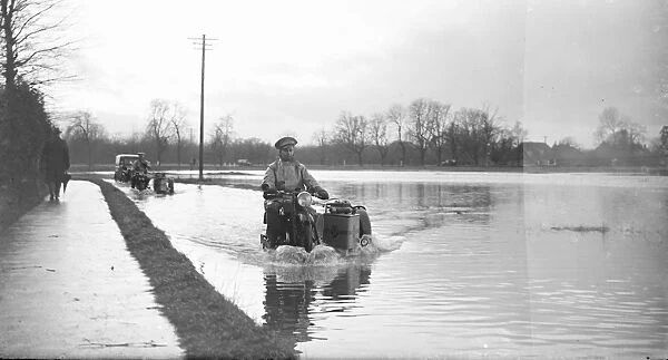 An AA Patrolman risks the flooded road on his motorbike. 1936
