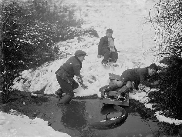Boys getting out of a stream after crashing into it on their toboggan