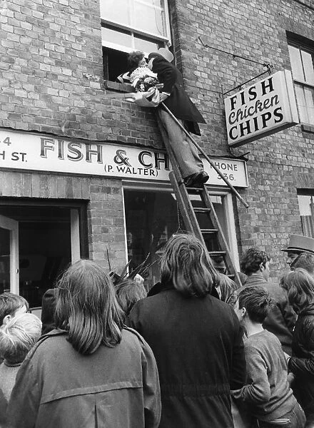 The bridegroom climbs a ladder to kiss his bride at the window above a fish and chip shop