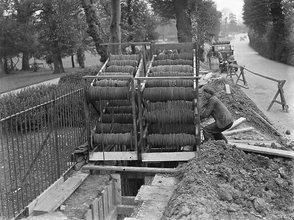 Bundles of telephone cables on a cradle that are being laid underground by workers