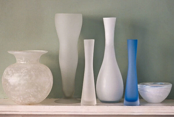 A collection of ground glass vases on mantel shelf, against, green wall credit