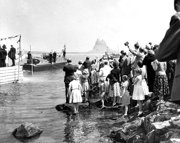 Crowds line the shore on Holy Island as the royal barge approaches the landing stage