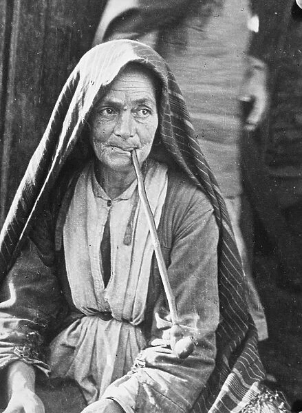 Elderly Jewish woman pipe addict of a Russian ghetto dressed in coarse cloths and shawl