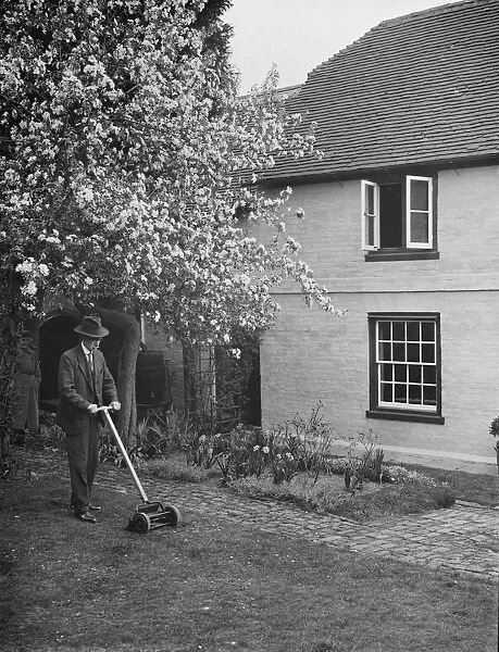 An elderly man cuts the grass at his cottage garden in Farningham, Kent. 7 April 1938