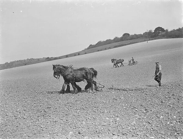 In the foreground a farmer uses a horse drawn harrow whilst behind you can see a
