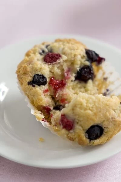 Fresh berry muffin with raspberries and blueberries, torn open on white plate