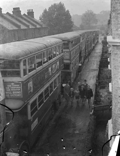 A group of children walking past a seriers of London Transport buses which are parked
