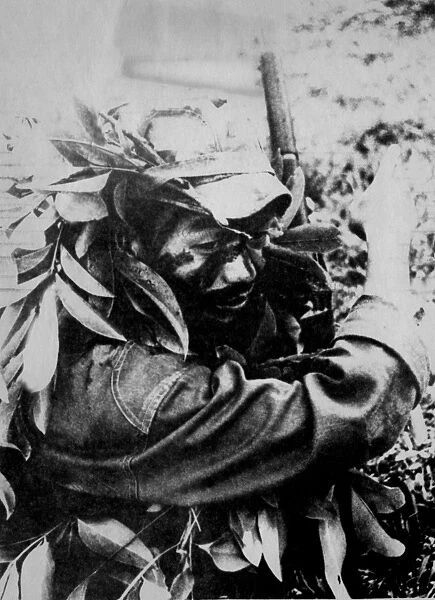 Jungle war in Laos: A Royal Laotian soldier, face blackened and headgear campouflaged with branches