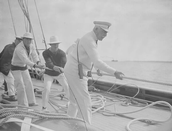 The King takes the wheel of his yacht Britannia. The Duke of Connaught lends