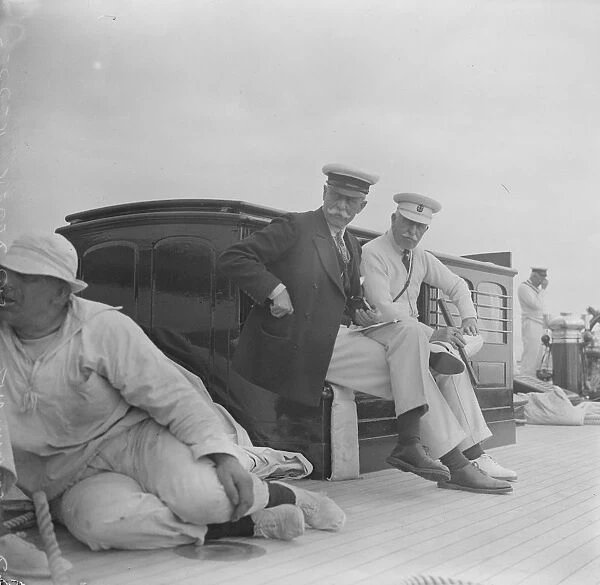 The King takes the wheel of his yacht Britannia. The Duke of Connaught and Sir