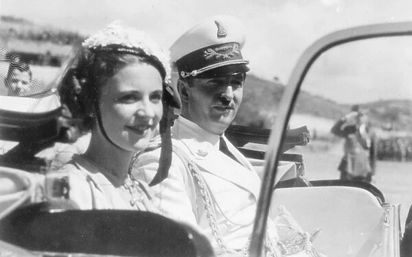 King Zog of Albania and his smiling young Queen, Geraldine, driving away after attending