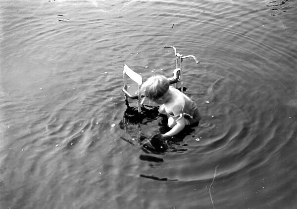 Little boy plays with a trike in the water. 1933