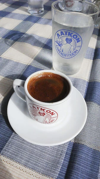 Little cup of strong Greek coffee, with glass of water on table of beach restaurant