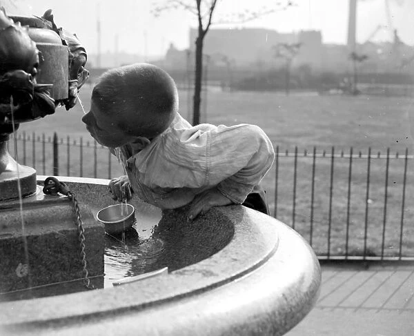 London summer. A little boy drinks water from a fountain. 1933