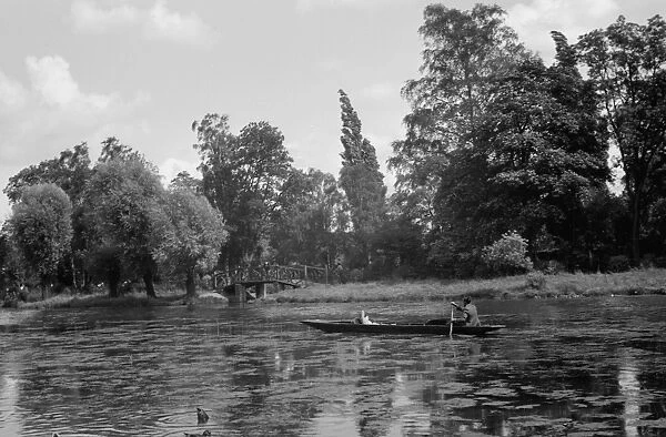 A man in his long boat rowing along the Boating Pool, Mill Garden, River Leam