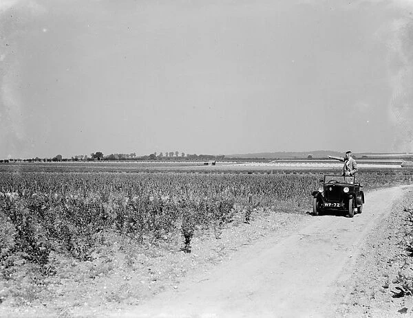 A man stands in his open top car, taking in the countryside scenery