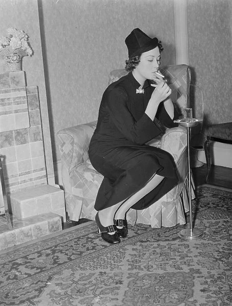 Miss Muriel Oxford sits by the fire having a cigarette