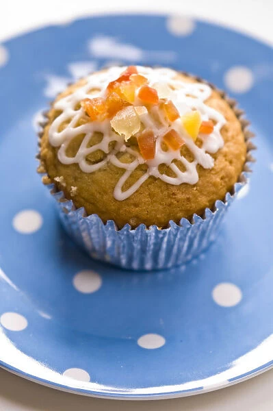 Muffin decorated with squiggly icing and candied peel on spotted blue plate credit