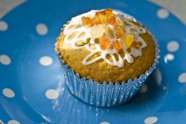 Muffin decorated with squiggly icing and candied peel on spotted blue plate credit