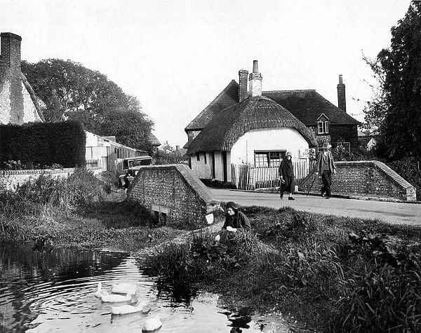 The old thatched cottage, the rippling stream, and a pretty girl feeding the ducks