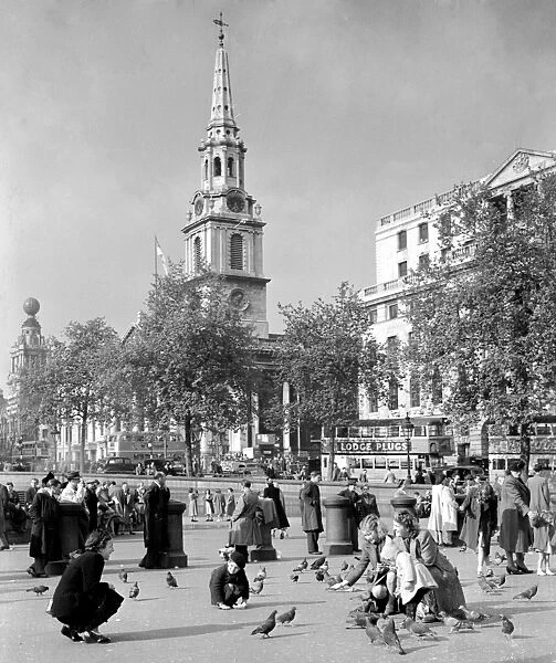People feeding pigeons in Trafalgar Square with the church spire of St Martin