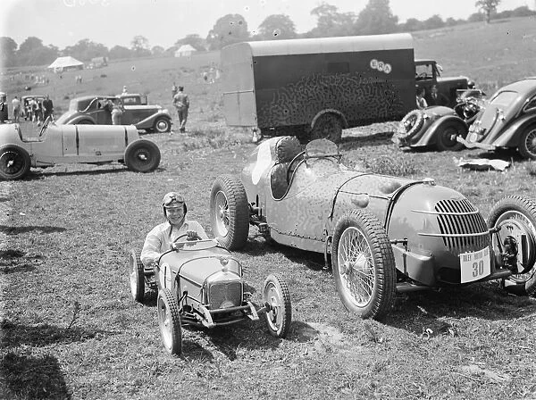 Peter McClure sits in a toy race car, parked next to the real thing, in Lullingstone