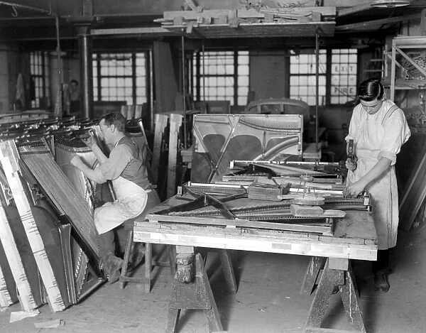 Piano making at Brinsmeads Factory. The man on the right is fitting in wires while
