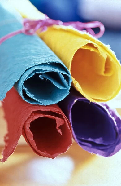 Four pieces of brightly coloured handmade paper rolled up and tied with pink string