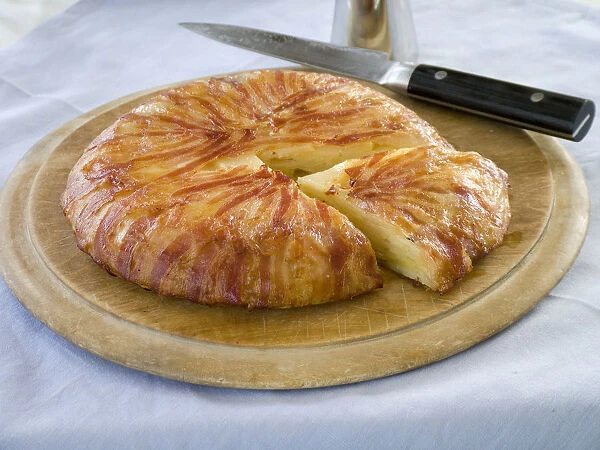 Potato galette wrapped in bacon on wooden board with knife credit: Marie-Louise