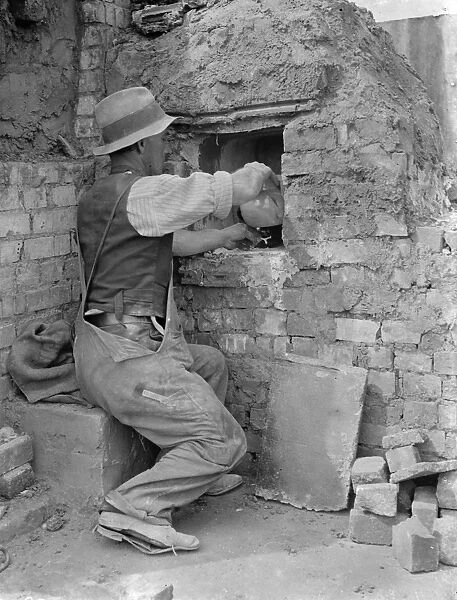 Pottery maker Mr Sadler filling clay into a kiln. 1938