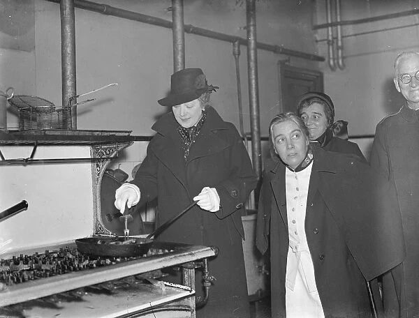 Premiers wife, fries sausages, during East end hostel visit. Mrs Neville Chamberlain