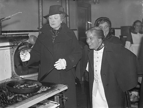 Premiers wife, fries sausages, during East end hostel visit. Mrs Neville Chamberlain