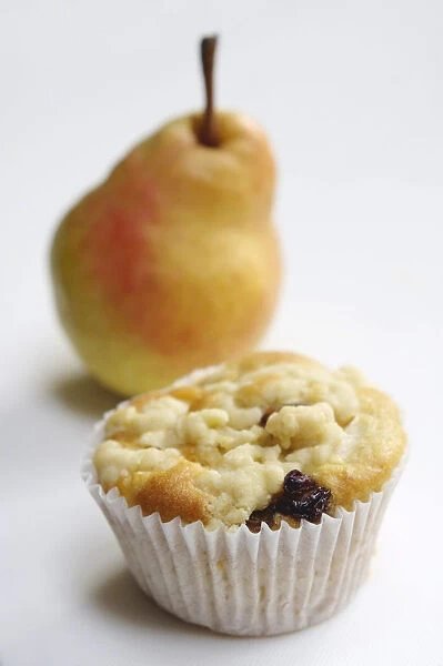 Raisin muffin in plain paper case, topped with grated pear and with whole pear behind