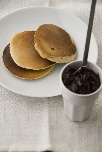Three Scotch pancakes on a white plate with small pot of raspberry jam credit