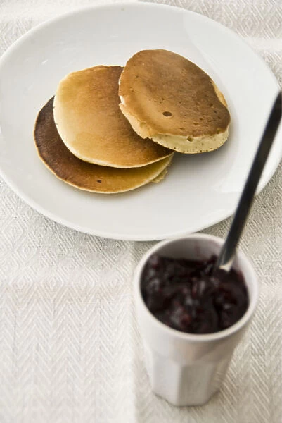 Three Scotch pancakes on a white plate with small pot of raspberry jam credit