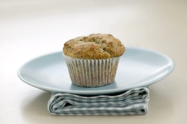 Single poppyseed muffin on blue plate on check napkin, on painted table. credit