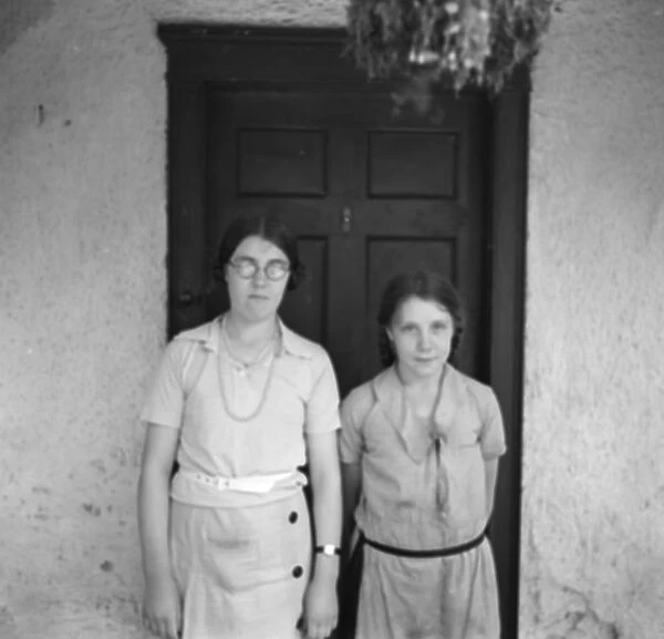 Two sisters pose in front of a cottage. 1936