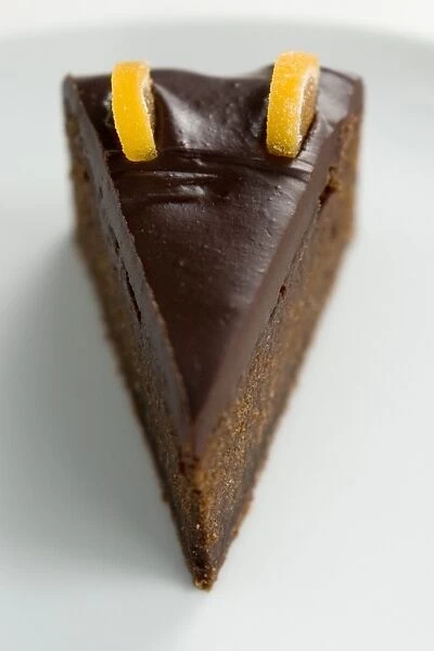 Slice of rich dense dark chocolate cake with shiny choc topping and candied orange