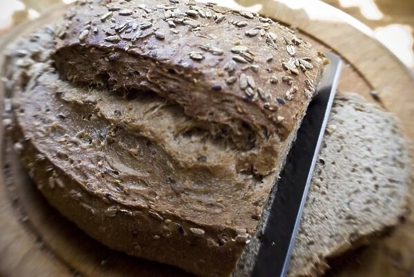 Slicing a wholegrain, rye and walnut loaf on old wooden board. credit: Marie-Louise
