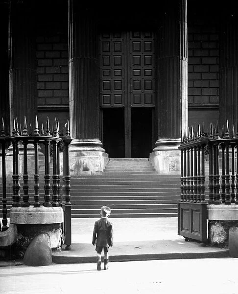 A small boy dwarfed by the imposing columns and steps to the entrance of St Pauls Cathedral
