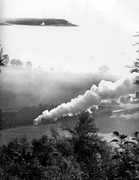 A steam train rattles through a misty valley