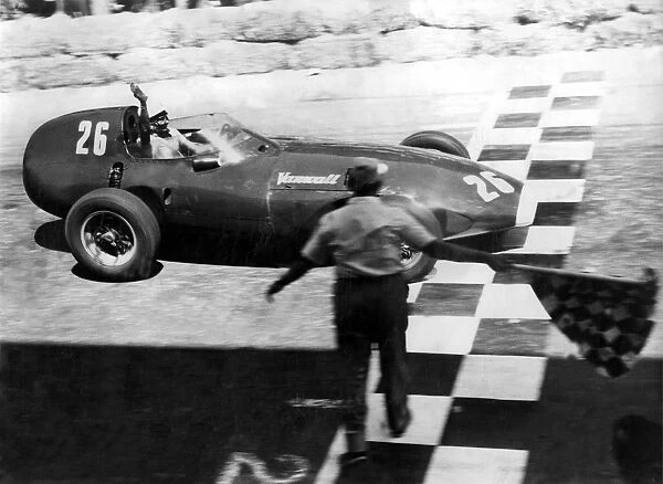 Stirling Moss raises his hand in salute as he crossed the chequered line to win the
