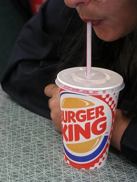 Sucking a soft drink out of a straw in a colourful Burger King disposable cup with a plastic lid