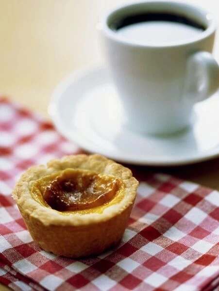 Traditional English custard tart on red gingham tablecloth with cup of black coffee credit