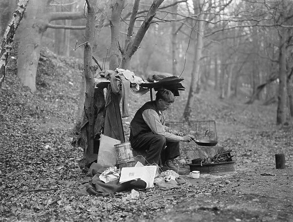 Tramp at home in woods cooking food over a camp fire. 1935