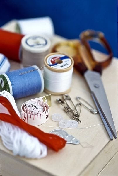Various bits of sewing kit, including threads, needles and scissors on wooden box