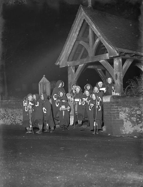 Young hooded carol singers singing by the lych gate outside Eynsford church, Kent