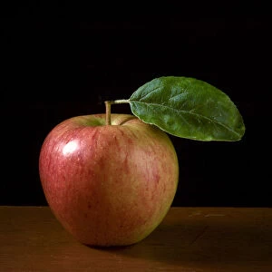Apple with leaf on wooden surface against black background credit: Marie-Louise