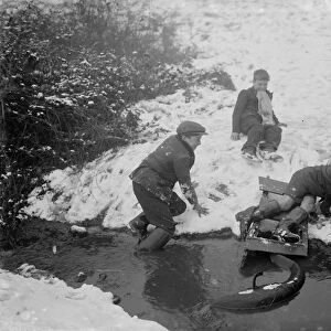 Boys getting out of a stream after crashing into it on their toboggan