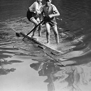 Boys have good fun with an improvised raft on the village pond at Orpington, Kent
